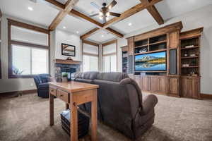 Living room with coffered ceiling, carpet flooring, a ceiling fan, a fireplace, and beam ceiling
