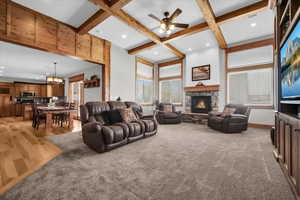 Living room featuring ceiling fan, a stone fireplace, coffered ceiling, beamed ceiling, and a chandelier