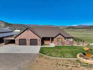 View of front of property featuring a mountain view, brick siding, concrete driveway, a garage, and a front yard