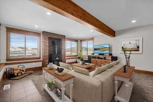 Living area with a wood stove, recessed lighting, light tile patterned flooring, and beamed ceiling