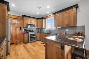 Kitchen featuring stainless steel appliances, light wood finished floors, a peninsula, tasteful backsplash, and dark stone countertops