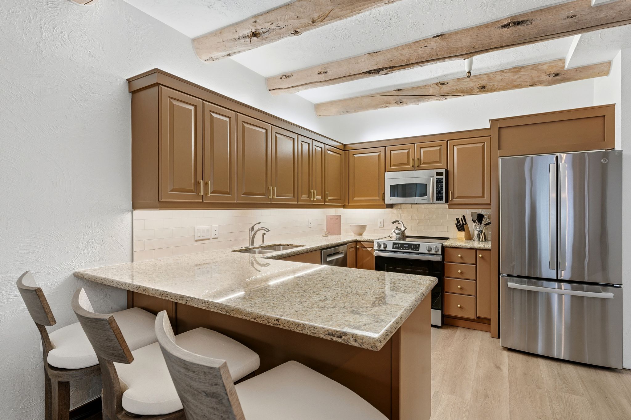 Kitchen with stainless steel appliances, a peninsula, a kitchen breakfast bar, light stone countertops, and beam ceiling