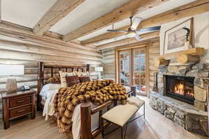 Bedroom with wood finished floors, a fireplace, rustic walls, beam ceiling, and access to outside