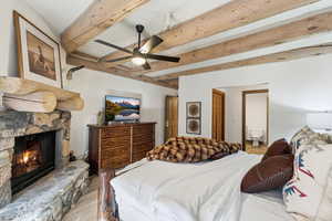 Bedroom featuring beam ceiling, wood finished floors, ensuite bath, ceiling fan, and a fireplace