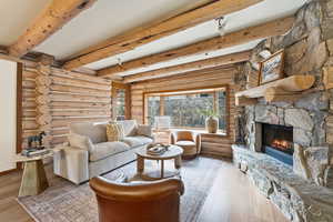 Living room with beamed ceiling, a fireplace, wood finished floors, and rustic walls