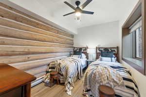 Bedroom featuring light wood finished floors, log walls, ceiling fan, and a baseboard heating unit