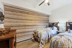 Bedroom with rustic walls, a baseboard heating unit, light wood finished floors, and ceiling fan