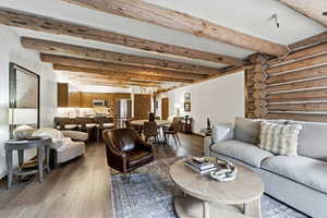 Living room featuring a chandelier, beam ceiling, dark wood-style flooring, and log walls