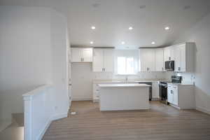Kitchen with light wood finished floors, a kitchen island, recessed lighting, appliances with stainless steel finishes, and white cabinetry
