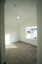 Carpeted empty room featuring visible vents, lofted ceiling, and baseboards