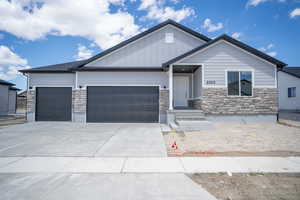 View of front of house with board and batten siding, concrete driveway, an attached garage, and stone siding