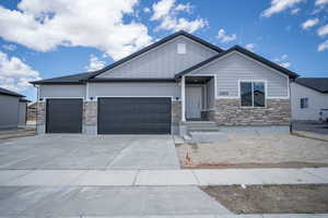 View of front facade with stone siding, driveway, board and batten siding, and an attached garage