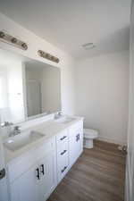 Full bathroom with double vanity, toilet, wood finished floors, and a sink