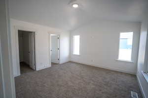 Unfurnished bedroom featuring a spacious closet, visible vents, baseboards, dark carpet, and vaulted ceiling