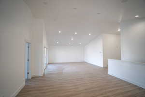 Unfurnished room with recessed lighting, high vaulted ceiling, baseboards, and wood finished floors
