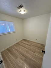 Unfurnished room with light wood finished floors, visible vents, a textured ceiling, and baseboards