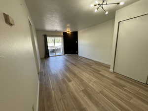 Spare room with a textured ceiling, wood finished floors, baseboards, and a chandelier