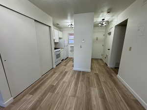 Kitchen featuring white appliances, a wall unit AC, a textured ceiling, white cabinetry, and light wood-type flooring