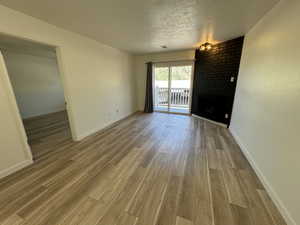 Empty room featuring a fireplace, wood finished floors, baseboards, and a textured ceiling