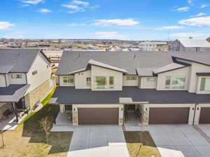 View of front of home with stone siding, an attached garage, driveway, and roof with shingles