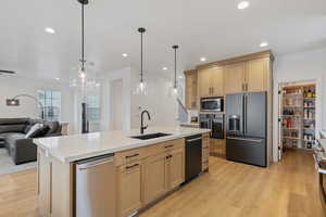 Kitchen with light brown cabinets, a sink, open floor plan, light wood-style floors, and appliances with stainless steel finishes