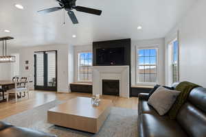 Living room featuring a wealth of natural light, a glass covered fireplace, light wood-type flooring, and ceiling fan