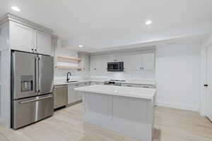 Kitchen with open shelves, stainless steel appliances, light countertops, and a sink