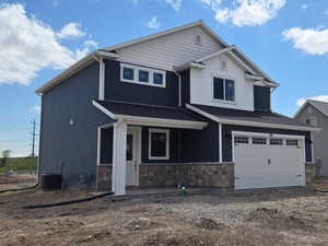 Craftsman house with central AC unit, stone siding, an attached garage, and driveway