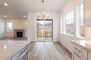 Kitchen featuring light wood-style flooring, white cabinetry, an inviting chandelier, a fireplace, and light stone countertops
