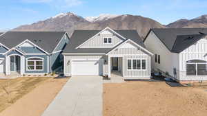 View of front of house with board and batten siding, roof with shingles, driveway, a garage, and a mountain view