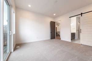 Unfurnished bedroom with visible vents, baseboards, recessed lighting, light carpet, and a barn door