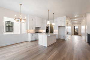 Kitchen with white cabinetry, a notable chandelier, tasteful backsplash, and appliances with stainless steel finishes