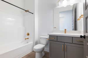 Bathroom with baseboards, toilet, bathtub / shower combination, wood finished floors, and vanity