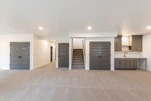 Unfurnished living room with stairs, recessed lighting, light colored carpet, and a sink