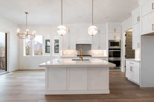 Kitchen with backsplash, appliances with stainless steel finishes, white cabinets, and light wood finished floors