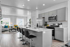 Kitchen featuring gray cabinets, appliances with stainless steel finishes, a breakfast bar area, and a sink