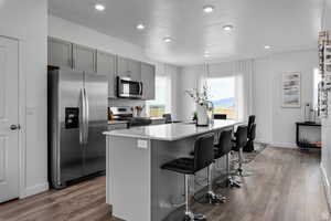 Kitchen with a center island with sink, a kitchen bar, gray cabinets, wood finished floors, and stainless steel appliances