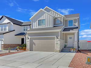 View of front of home with board and batten siding, concrete driveway, a garage, stone siding, and a gate