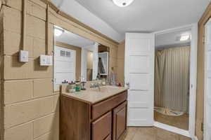 Full bath with tile patterned floors, vanity, concrete block wall, and a textured ceiling