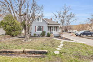 Bungalow with a front lawn, covered porch, roof with shingles, and a chimney