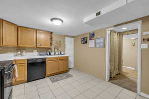 Kitchen with black appliances, tile counters, a textured ceiling, concrete block wall, and a sink