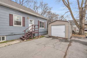 View of front of house with a shingled roof, a detached garage, a storage shed, an outdoor structure, and driveway