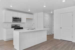Kitchen with light wood-style flooring, white cabinetry, stainless steel appliances, and a sink