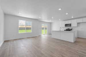 Kitchen featuring light wood-style flooring, a sink, open floor plan, white cabinetry, and appliances with stainless steel finishes