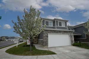 View of front of home with an attached garage, stone siding, a front lawn, and concrete driveway