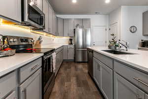Kitchen featuring gray cabinets, a sink, stainless steel appliances, light countertops, and dark wood-type flooring