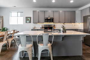 Kitchen featuring gray cabinetry, a kitchen bar, light countertops, stainless steel appliances, and dark wood-style flooring