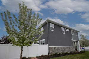View of property exterior featuring stucco siding, fence, and stone siding