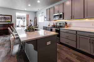 Kitchen featuring gray cabinetry, dark wood-type flooring, recessed lighting, a kitchen breakfast bar, and stainless steel appliances