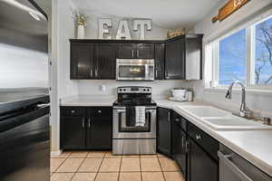 Kitchen featuring a sink, dark cabinetry, appliances with stainless steel finishes, and light tile patterned floors
